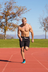 Obraz premium Male Athlete sprinting on a tartan athletics track on a bright s
