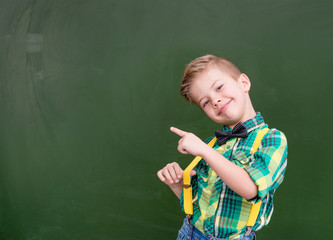 Young boy points on empty green chalkboard