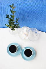 Two blue coffee cup on the table with a vase and saucer with marshmallows