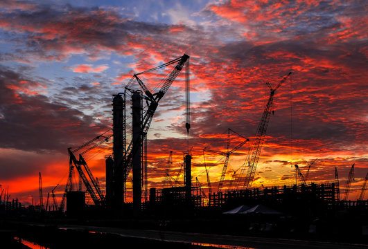 Silhouette shot of multiple cranes in construction sites with beautiful twilight sky.