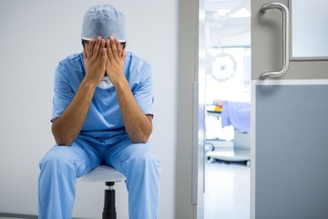 Tensed surgeon sitting with hands on face in corridor