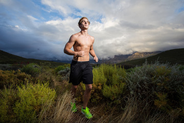 Male fitness model running allong a trail in the field, bare che