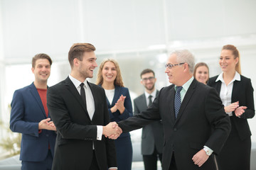 Two cheerful business people shaking hands while their colleague