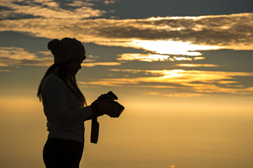Fototapeta premium Silhouette of a woman photographer standing in dry grass field on sunrise