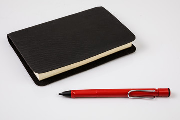 Black notebook with red pen or pencil on white background isolated.