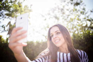 Pretty young millennial female model talking on her smart phone outside and taking selfies on her smart phone for social media