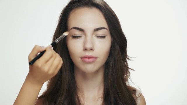 Make up artist applying eyeshadow on eyelid of a female model
