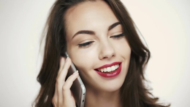 Smiling young brunette woman with purple lipstick talking on mobile phone