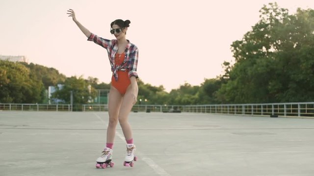 Young pretty brunette girl in sunglasses and red swimsuit skating wearing roller blades on the open road outdoors