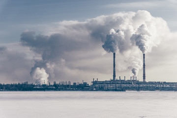 Power station with pipes of which poured smoke on a frozen river. Free copyspace