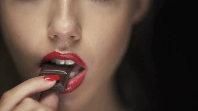 Young woman with red lipstick biting dark chocolate