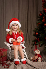 little girl in a Santa suit near Christmas tree
