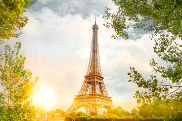 Fototapeta na wymiar View on Eiffel tower through green trees with cloud bckground. Eiffel Tower from Champ de Mars, Paris, France.