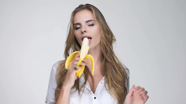 Pretty young woman in white shirt eating banana