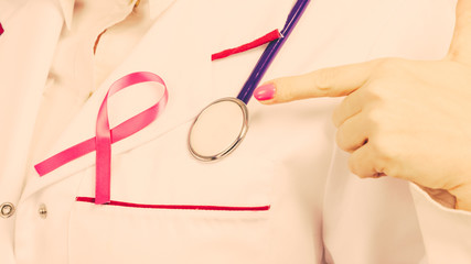 Pink ribbon with stethoscope on medical uniform.