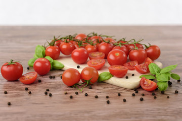 Scattered cherry tomatoes and pepper balls with leaves of basil on the wooden table. 
