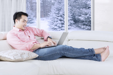 Naklejka premium Man typing with laptop on sofa