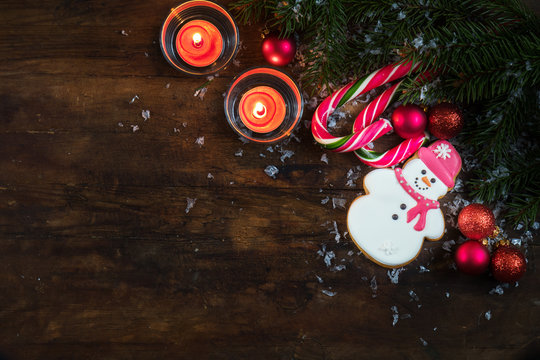 Christmas and New Year composition. Gingerbread snowman, fir tree branches, balls, light two candles and candy cane with snow on dark wooden background.