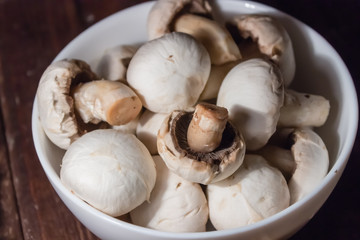 peeled mushrooms in a white bowl on wooden background