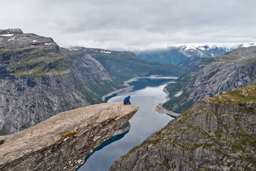 Fototapeta na wymiar Man sitting on Trolltunga rock (Troll's Tongue rock) and looking at Norwegian mountain landscape