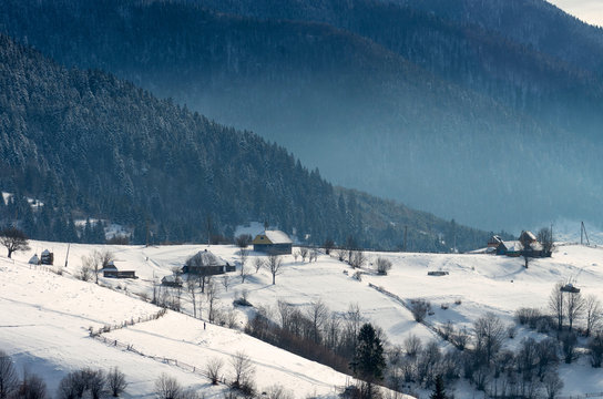 Little Farm on the edge of a winter forest. Winter mountain landscape with haze.