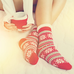 Young woman in Christmas pattern socks holding a mug with tea or coffee