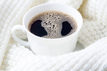 White cup of hot coffee surrounded by a white woolen scarf