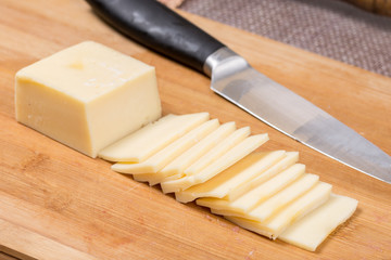 Sliced yellow cheese on the kitchen wooden board with knife