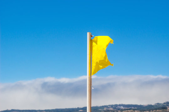 Yellow flag waving in the breeze against a blurred blue sky.