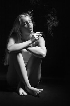young woman sitting in dark smoking cigarette, monochrome