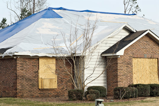 tornado damaged brick house with a tarp on the roof