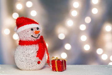 Snowman with red gift box on lights background.