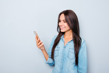 Naklejka premium Smiling girl reading message on mobile phone on gray background