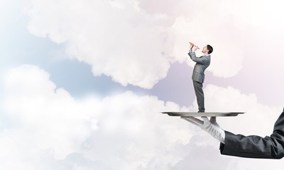 Businessman on metal tray playing fife against blue sky background