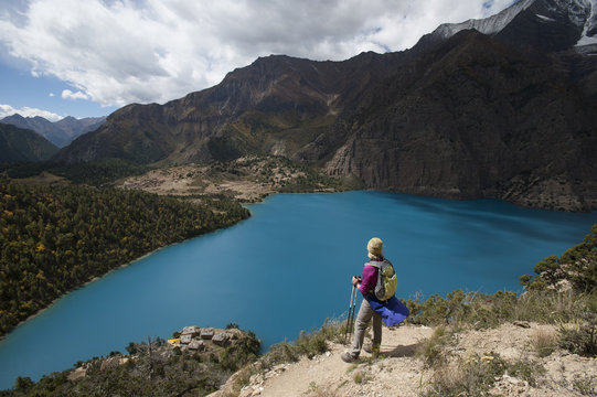 A trekker stands above the turquoise blue Phoksundo Lake in the Dolpa region, Himalayas, Nepal