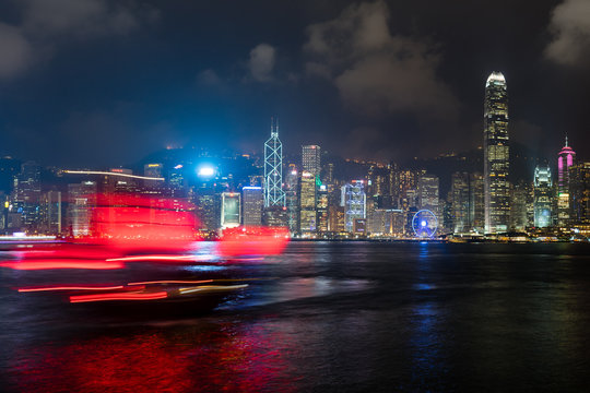 A red junk sailboat glides in front of the Hong Kong skyline at night, Hong Kong, China