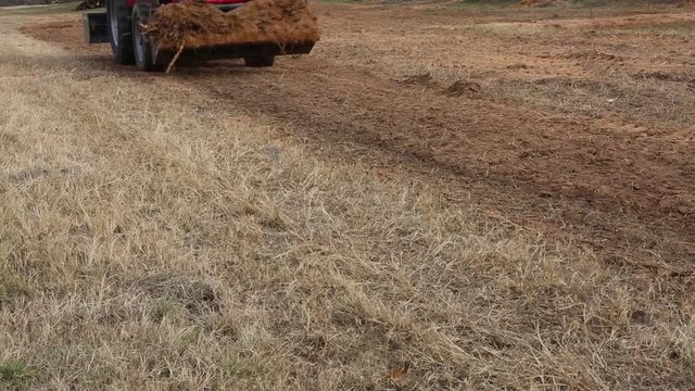 Red tractor passing by with a front end loader full of dirt.