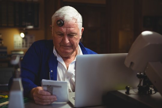 Horologist looking at notepad with laptop on table