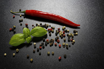 red chili pepper and basil leaves on black background