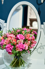 Bouquet of roses in a clear, circular, glass vase is on the table with a mirror.