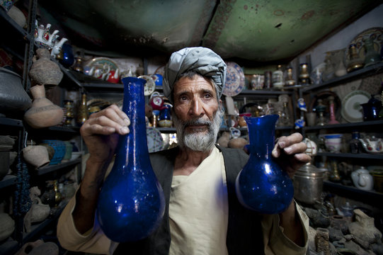 A Glass Blower Holds Up Blue Glass Gourd-shaped Vases In A Trinket Shop In Herat, Afghanistan