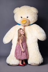 Little girl in dress standing near the large teddy bear