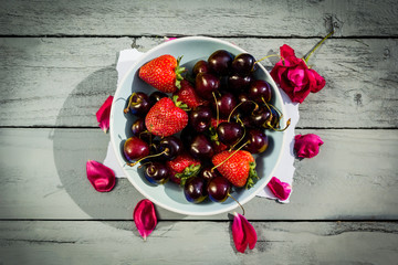 A bowl of cherries and and red roses on wooden background