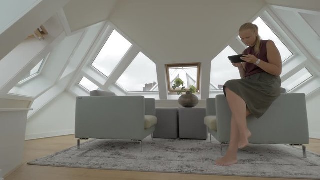 View of young blond woman sitting on the side of arm chairs using tablet inside of room in a Cube house. Unusual geometric form space, Rotterdam, Netherlands