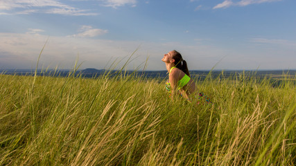 Young girl in colored clothing makes yoga on a mountain