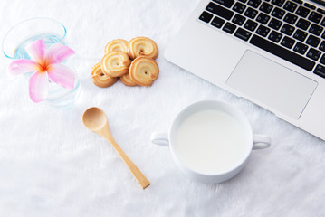 Table at the cafe with a cup of coffee, cookies and a laptop next to a window..