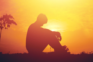 Silhouette of a young boy sitting sadly on sunset.