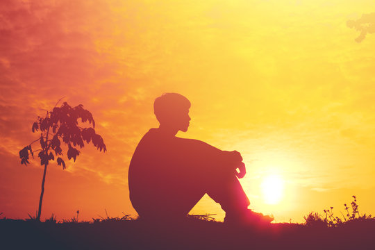 Silhouette of a young boy sitting sadly on sunset.