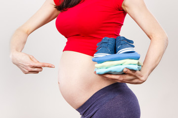 Pregnant woman showing clothing for newborn, expecting for baby