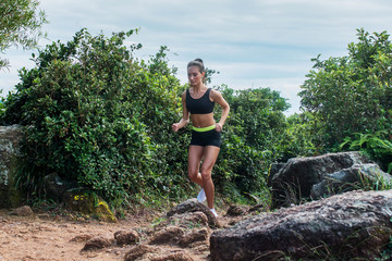 Fit athletic young woman running on dirty rocky path in mountains in summer.